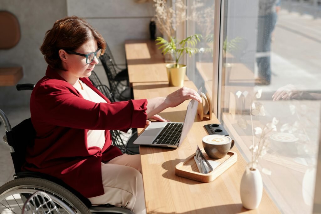 pexels-photo-4063619-4063619 Woman in wheelchair working on a laptop in a bright café, showcasing remote work lifestyle.